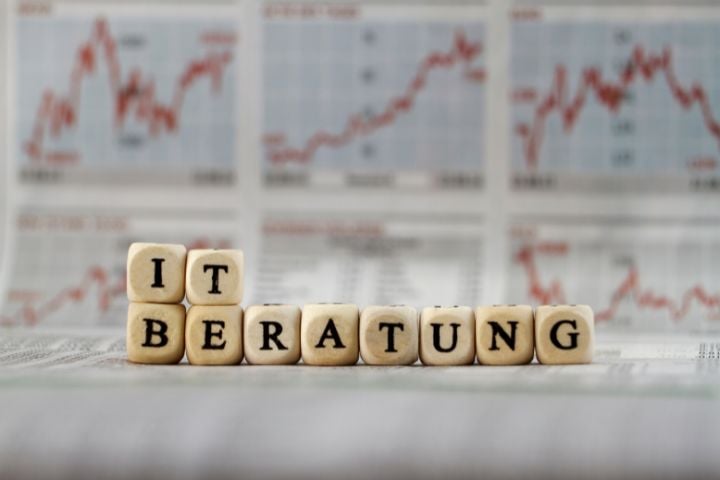 IT consulting with wooden letters in front of stock market charts and share prices
