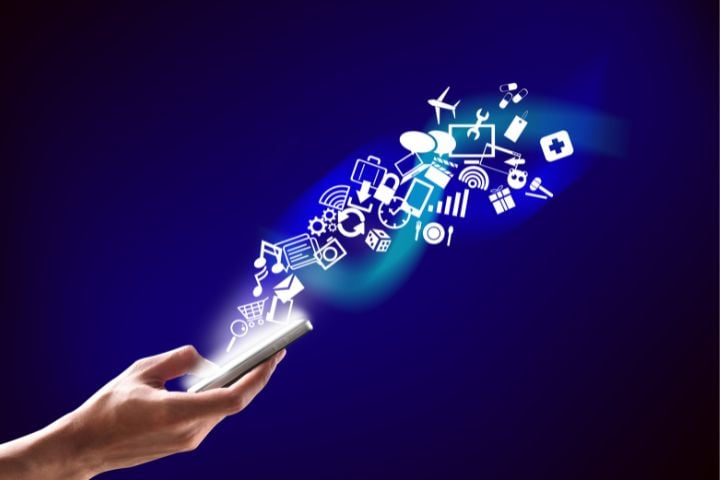 A hand holding a phone and apps symbolically flying out of it.