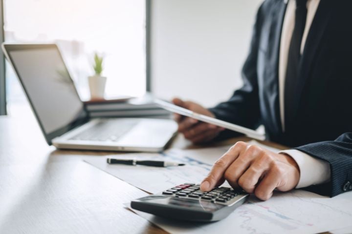 Business person in suit working on accounting with Sage 100 on a calculator, laptop in the background, emphasizing professional accounting in Switzerland.