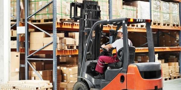 Logistics employee drives forklift truck in modern warehouse with high racks